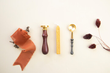 Gold sticks of sealing wax, orange silk ribbon, wax seal, dried flowers on pastel beige background. Top view, flat lay, copy space.