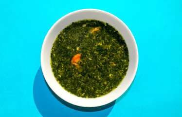 Molokhia soup with shrimps on blue background. Flat lay, top view. Moroheiya, Mulukhiya