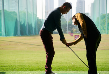 Asian coach mentoring golf player practicing swing at driving range