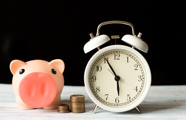 a stack of coins, a white alarm clock and a piggy bank on the table with a black background on the back