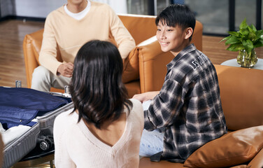 Asian kid and parents sitting in living room smiling talking to each other when packing suitcase preparing for travel