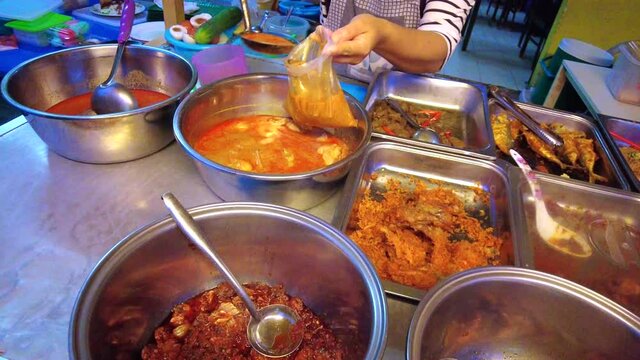 Seller is packing one of the various types of breakfast lauk or dishes at the Malaysian food stall. Footage may contain noise due to low light.