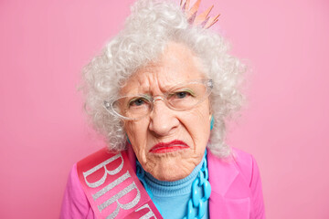 Close up shot of displeased wrinkled grandmother smirks face looks unhappily at camera has bright...