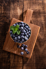 Bowl of fresh blueberries on rustic wooden board. Organic food blueberries and mint leaf for healthy lifestyle.