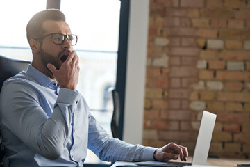 Office worker looking tired while using his laptop