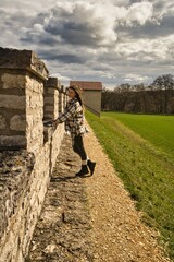 Fotografie von einer jungen Frau die an einer Steinmauer lehnt an einem schönen Frühlingstag.