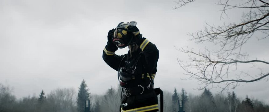 Hero shot, portrait of tired American female firefighter standing taking off her protective helmet, looking into camera. Shot with 2x anamorphic lens. 100 FPS slow motion