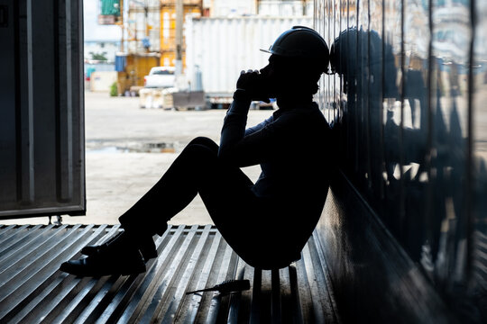 Depressed and tried foreman or businessman sitting inside the container in shipyard logistic factory because losing his job or fired because of mistake. Worker or officer feeling sad and depressed.
