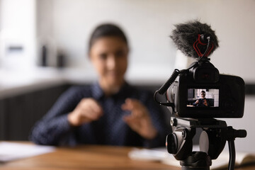 Close up Indian blogger using professional digital camera, recording video, tutorial or vlog, sitting at work desk, young woman teacher business coach shooting webinar, speaking, explaining,