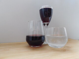 two glasses of red wine and a glass of water on a wooden table.