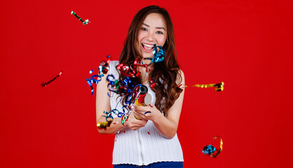 Funny young and cure Asian girl holding and blowing out party poppers with funny and happy. Studio shot on red background