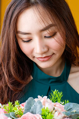 Obraz na płótnie Canvas Close up face shot of cute and pretty curly hair Asian female brunette holding flower bouquet with cheerful and happy, studio shot isolated on bright yellow background.