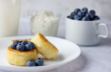 Cottage cheese pancakes with blueberry, sour cream and glass of milk on stone background.