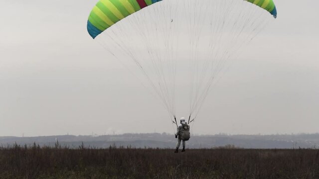 Paraglider landing on a withered autumn field on cloudy sky background. Action. Parachutist ends his flight successfully.