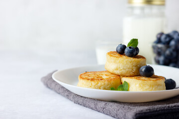 Cottage cheese pancakes, syrniki, curd fritters with fresh blueberries and milk on light background. Copy space for your text. Russian breakfast menu.