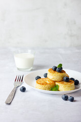 Cottage cheese pancakes, syrniki, curd fritters with fresh blueberries and milk on light background. Copy space for your text.