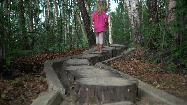 Barefoot preschooler girl walking on tree stumps. Sensory feet massage path