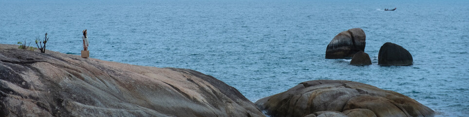 A woman standing on the rock by the seashore with blue sky background