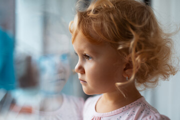 Close-up portrait of sad children girl looking through window.