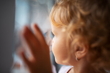 Fototapeta premium Close-up portrait of children girl looking through window.