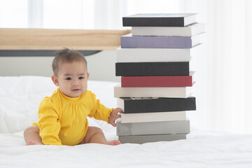 Portrait baby child sitting on bed near books are put on bed height more than baby is sitting. Baby child are smiley look happy in bedroom in the morning