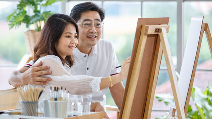 Senior man and woman couple, husband and wife, painting image together in home gallery with warm and happy circumstance. The man holds woman with love and care.