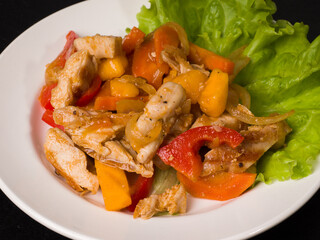 Hot meat salad. Chicken, pepper and persimmon pieces on a white plate. Studio photography