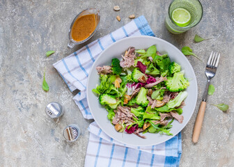 Healthy salad with boiled broccoli, duck, fried mushrooms and peanut dressing in a gray plate on a light concrete background. Salad recipes.