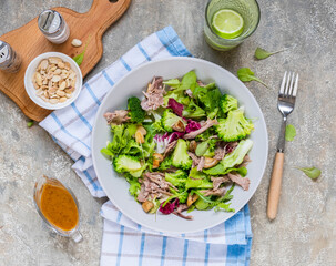 Healthy salad with boiled broccoli, duck, fried mushrooms and peanut dressing in a gray plate on a light concrete background. Salad recipes.