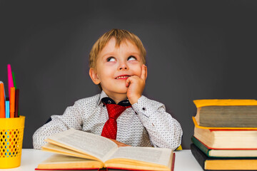 pensive preschool boy sitting at a Desk. Blond boy does his homework