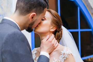Young loving bride and groom hug and kiss near the blue windows