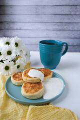 Cheesecakes, cottage cheese or ricotta pancakes served with sour cream on a light background, copy space. Russian, Ukrainian cuisine sweet food. 