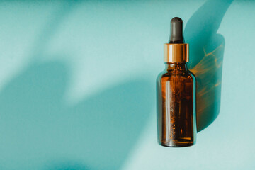 Bottle of essential oil on bright blue background with shadows