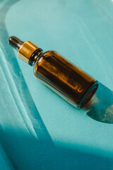 Bottle of essential oil on the water on blue background with shadow