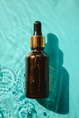 Bottle of essential oil on bright blue background with shadow of whater waves