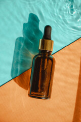 Bottle of essential oil on bright blue and orange background with shadow of whater waves