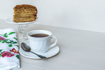 White cup of tea with a spoon. A piece of honey cake in the background.