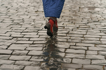 Young trendy woman walking at the Moscow Red Square. She wear red boots with high heels. Dull spring day. Cold. Pavement is wet, slippery after night frost and rain in the day. Traveling concept