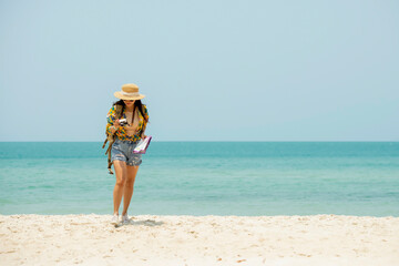 Asian woman traveler with backpack holding camera and map walking on the beach enjoy life