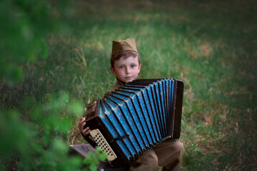 A boy in a military uniform with an accordion in nature