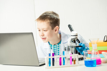 Schoolboy with a laptop in the laboratory conducts chemical experiments with substances in test tubes, portrait of a young chemist