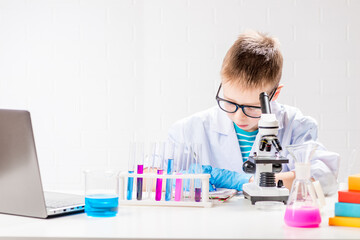Fototapeta premium A schoolboy with a microscope examines chemicals in test tubes, conducts experiments - a portrait on a white background. Concept for the study of coronavirus in the laboratory