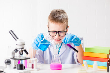 A schoolboy with a microscope and book examines chemicals in test tubes, conducts experiments - a...