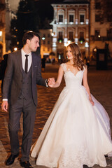 Naklejka premium Happy newlyweds walk holding each other's hand on the ancient street of the European city.