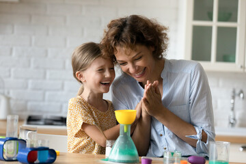 Smiling little girl child have fun playing chemistry lab childish game with young mother at home....