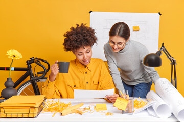 Cheerful mixed race women coworkers discuss ideas for project share opinion with each other prepare...