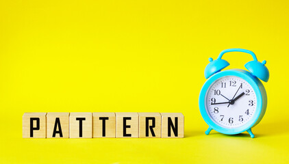 The word PATTERN is written on wooden blocks and on a yellow background, next to an alarm clock