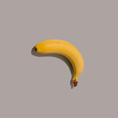 Yellow banana on a grey background. Playful minimal food concept. Unique abstract flat lay idea.