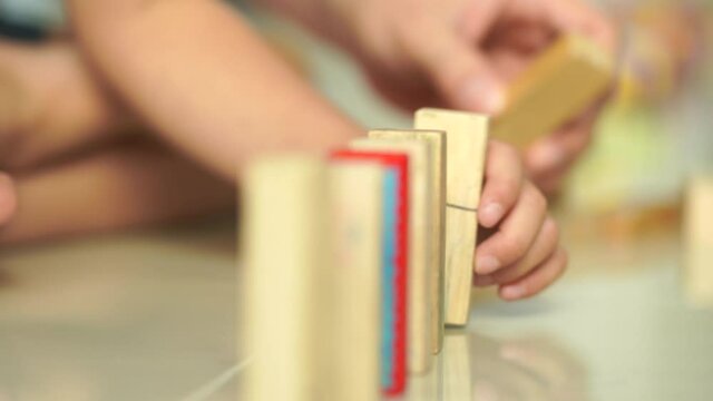 The father and son were having fun on vacation. One family was helping to raise domino intently. The hands of two boys and the hands of a man were enjoying a game of falling domino.