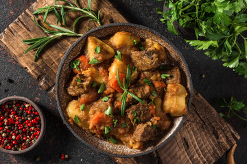 Stewed meat with potatoes, herbs and carrots in a plate on black background. top view